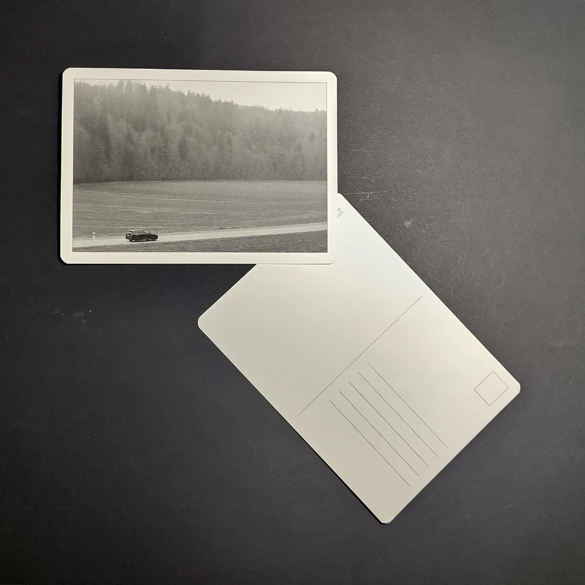 September Postcard - Black-and-white photo of a car driving along a misty country road bordered by forest